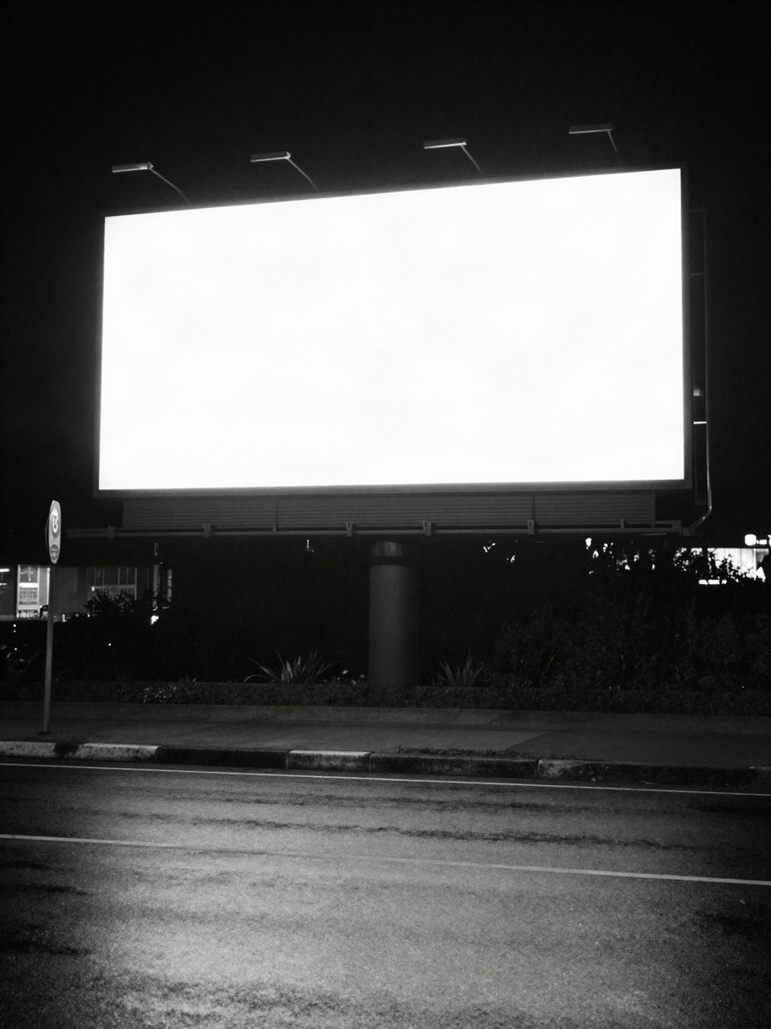 An empty billboard lightbox glowing blank white against a dark night sky on a city street, wet road reflecting the light.